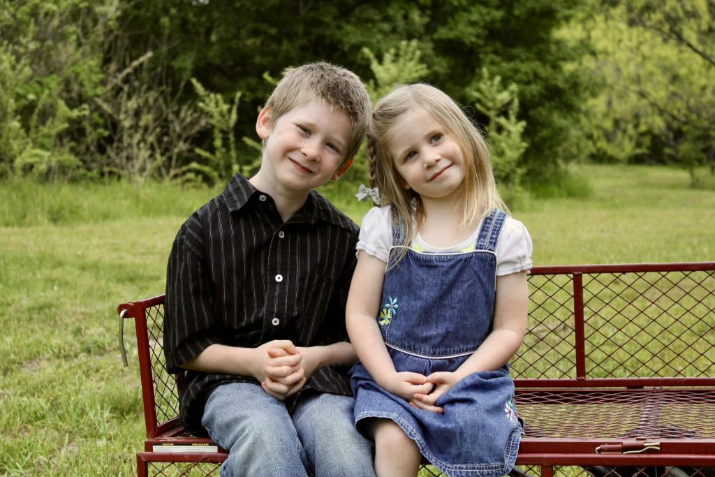 Emma and Kaleb sit next to each other on a bench for a photo. Both are young children smiling at the camera.