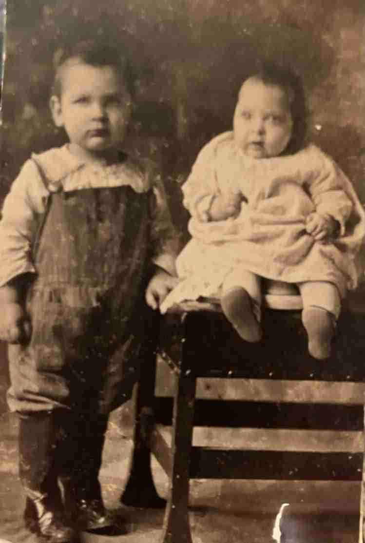 An old black and white photograph shows two children posing for the camera